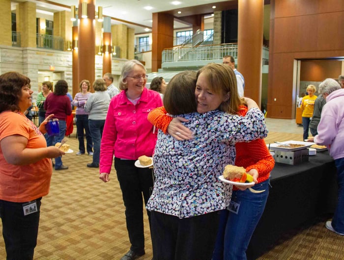 Associates embrace each other while attending anniversary celebration.