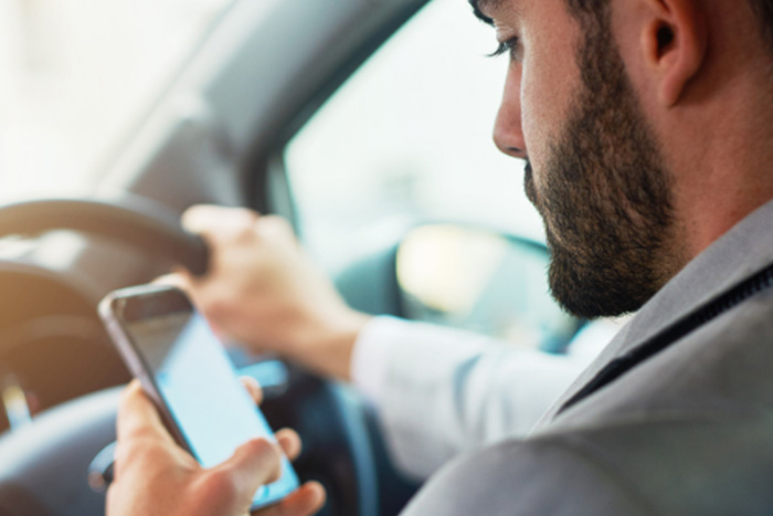 Man looks down at cell phone while driving.