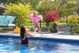 Young girl jumps into the pool while her mother stands by to catch her.