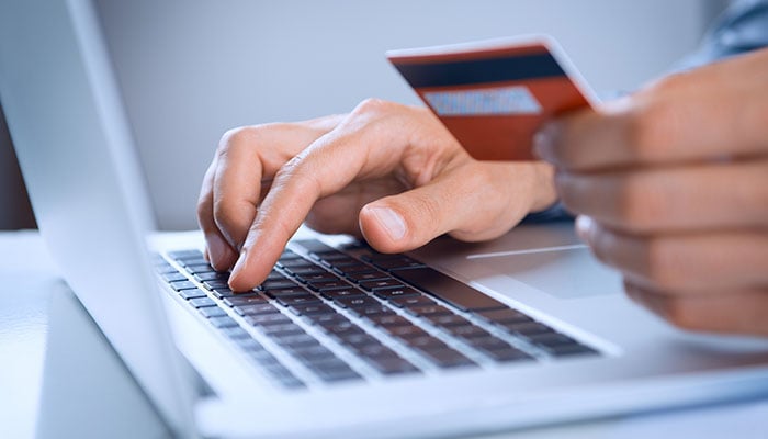 close up of man holding credit card while typing on keyboard