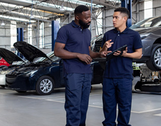 Team of mechanics discussing the diagnosis of a car at an auto repair shop and using a digital tablet