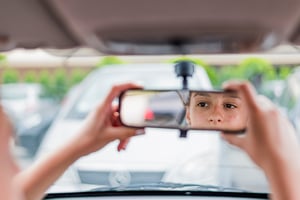 Teen girl adjusting rearview mirror during the day while driving her car.
