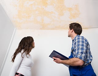 Man and woman look up at the ceiling damage in home