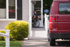 Man in a wheelchair going up home ramp and in the door