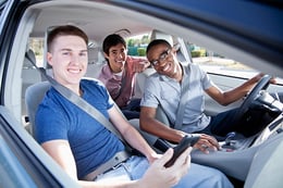 Three teens smiling and wearing seat belts inside car.
