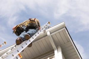 Man standing on ladder while checking on house roof.