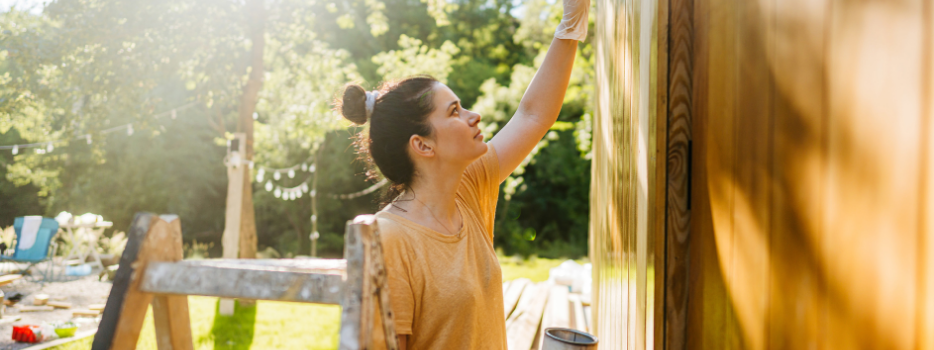 A woman staining a small building outside