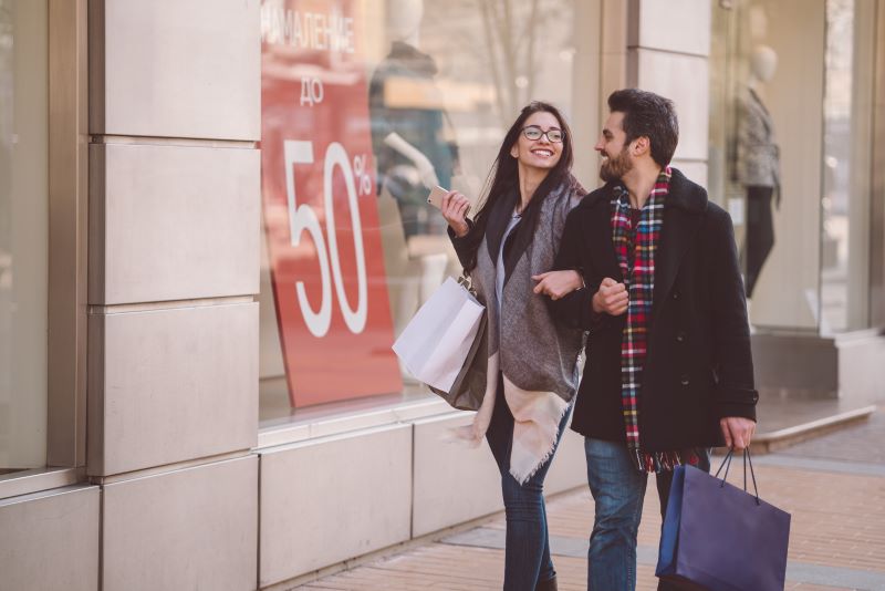 Couple walks down the street linking arms while out shopping.